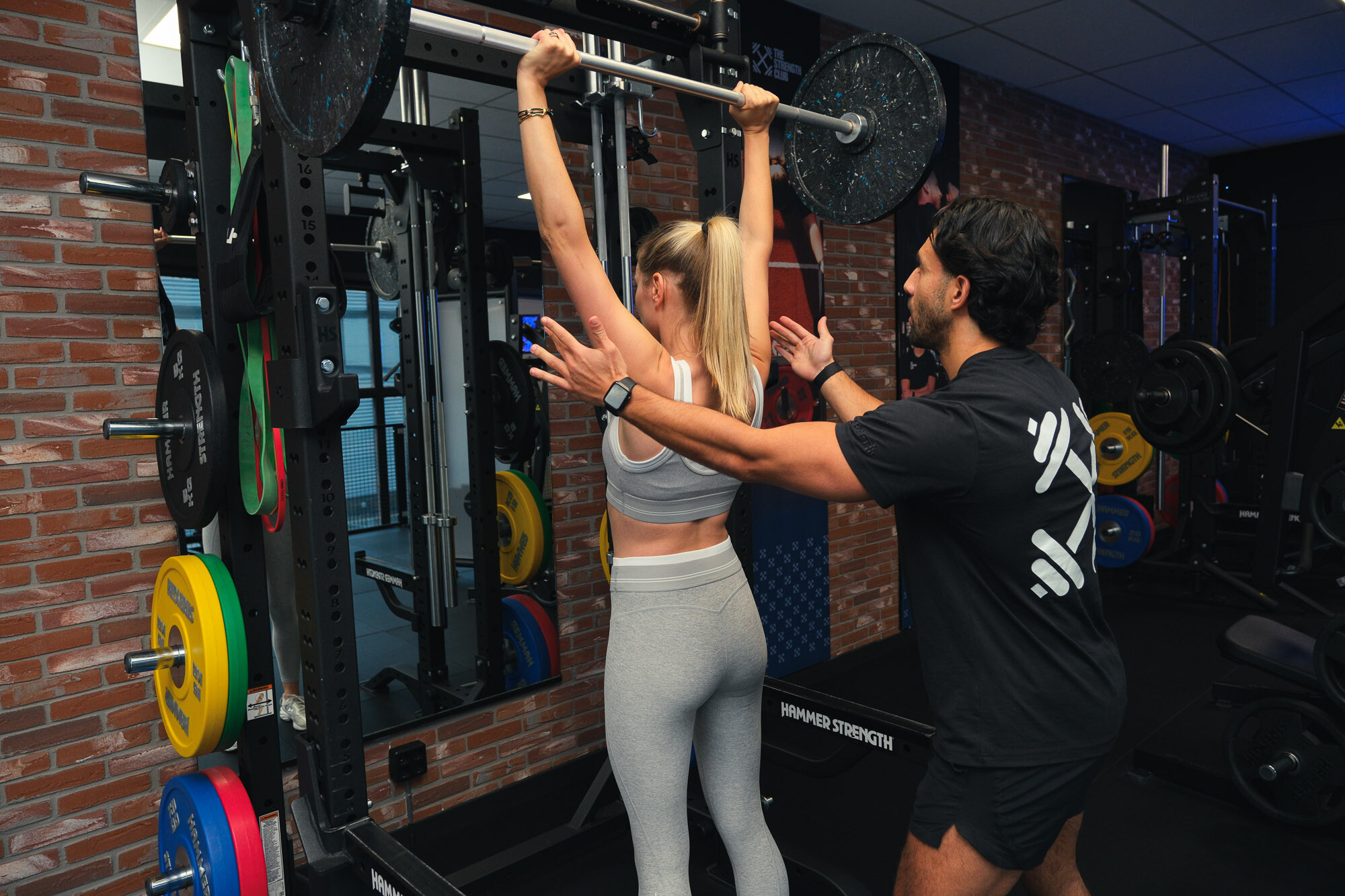 Personal trainer begeleidt een sporter bij een schouder press met halterstang Personal trainer begeleidt een sporter bij een schouder press met halterstang