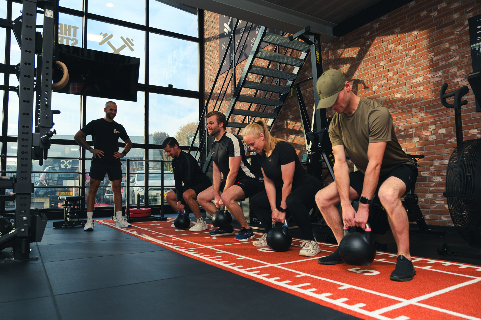 Groep sporters traint met kettlebells op de oranje sprintbaan