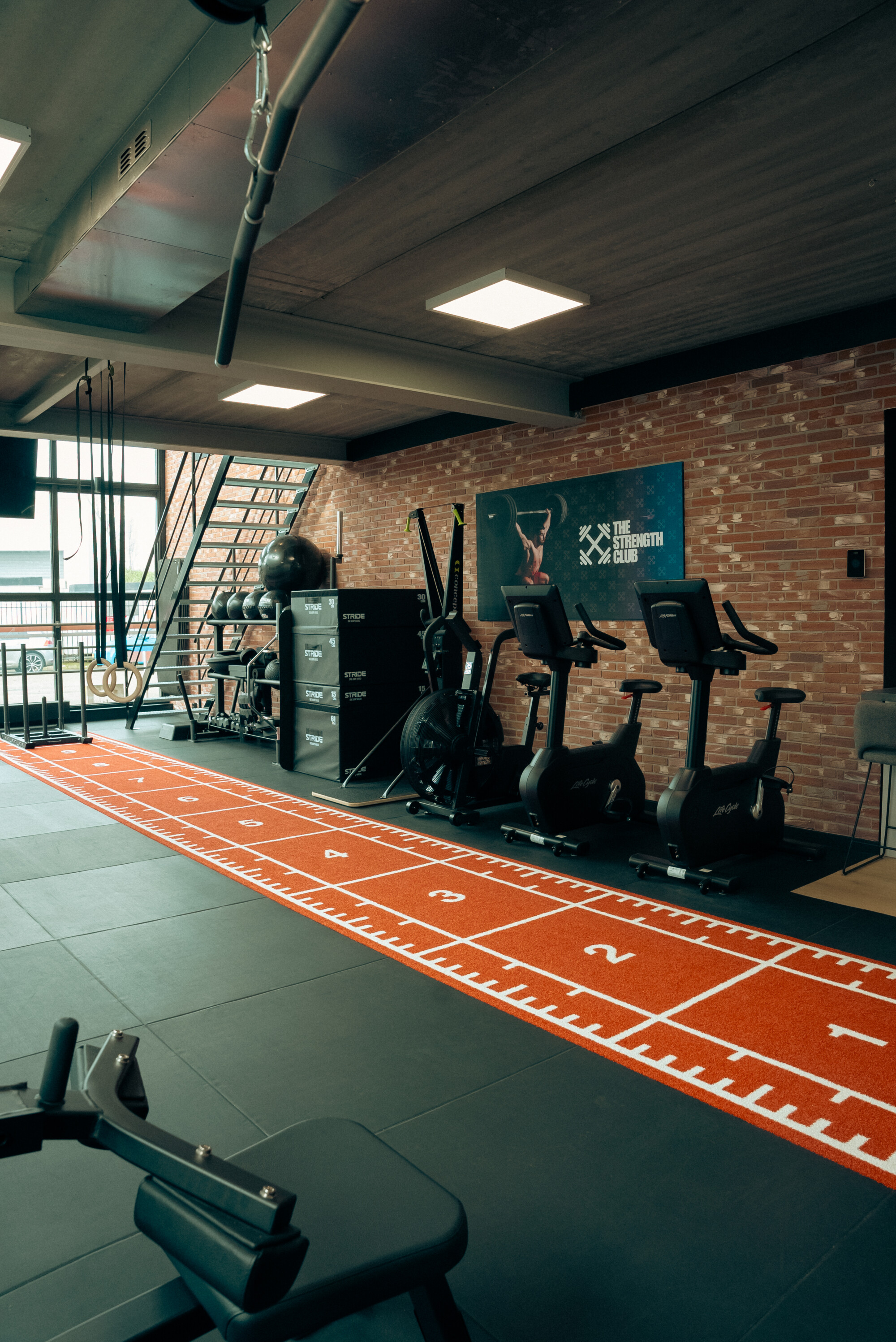 Trainingsruimte met cardiotoestellen en een oranje sprintbaan bij The Strength Club. Trainingsruimte met cardiotoestellen en een oranje sprintbaan bij The Strength Club.