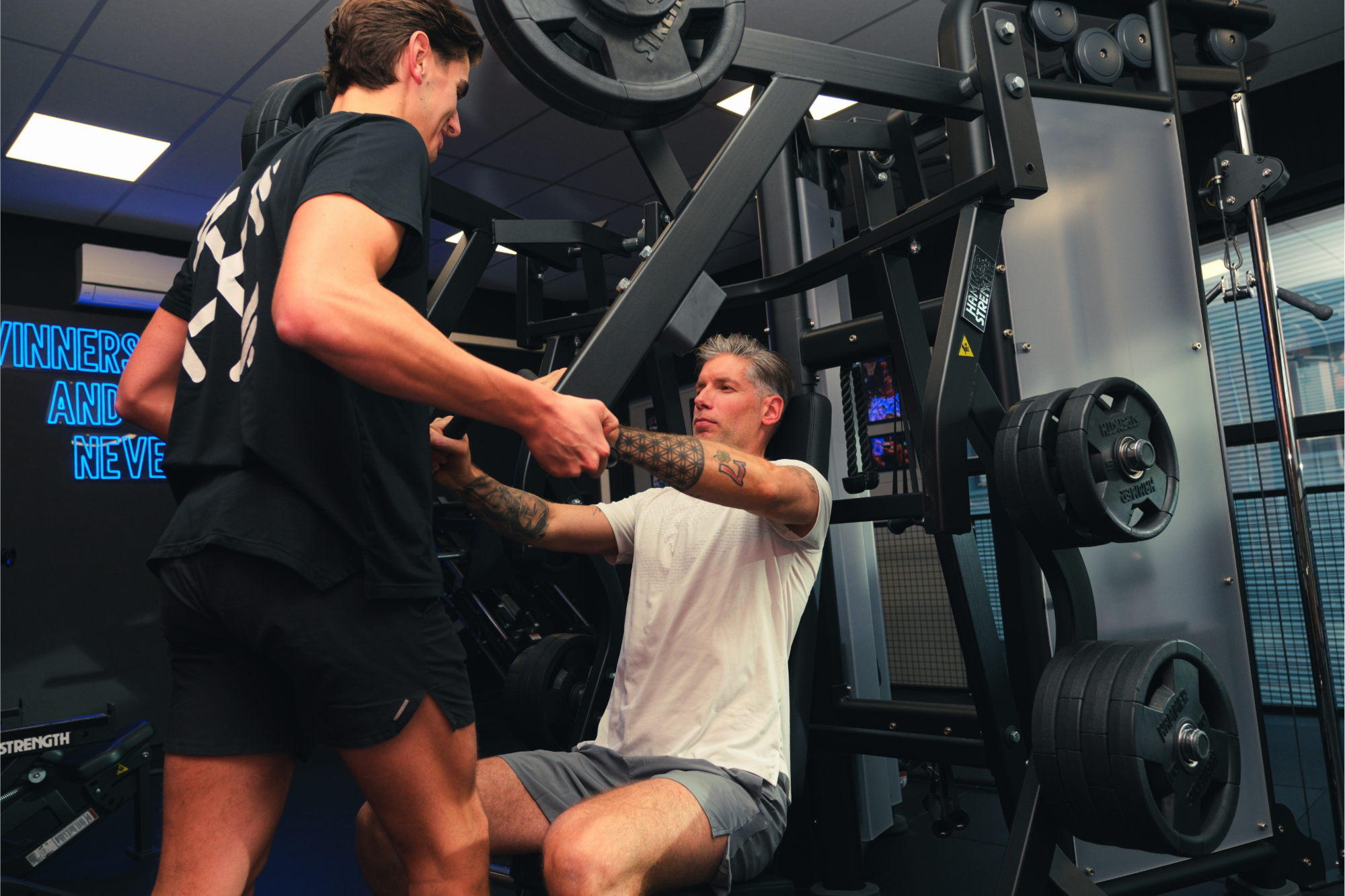 Personal trainer begeleidt een sporter bij een chest press machine Personal trainer begeleidt een sporter bij een chest press machine