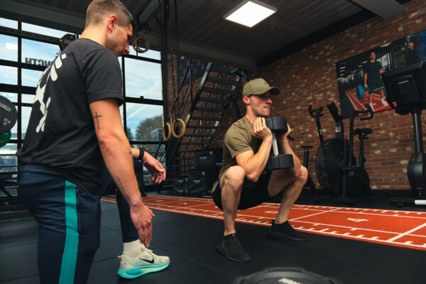 Personal trainer begeleidt een sporter bij een goblet squat