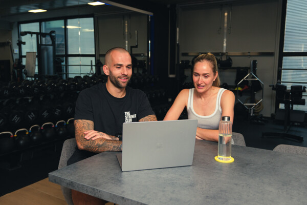 Personal trainer en sporter bekijken samen een trainingsschema op een laptop aan de bar