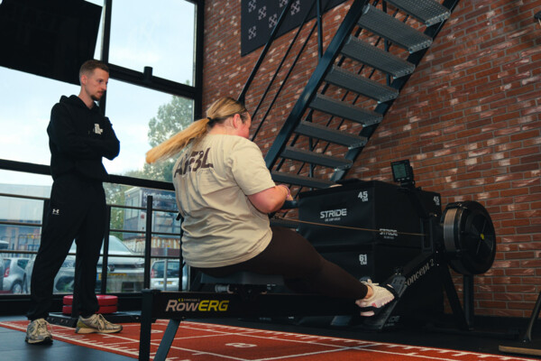 Personal trainer begeleidt een sporter op de roeimachine