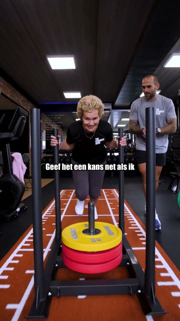 Sporter duwt een verzwaarde slee onder begeleiding van een personal trainer Sporter duwt een verzwaarde slee onder begeleiding van een personal trainer
