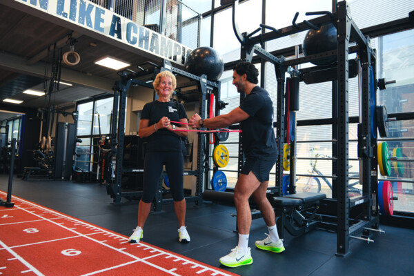 Personal trainer begeleidt een sporter bij een oefening met een weerstandsband