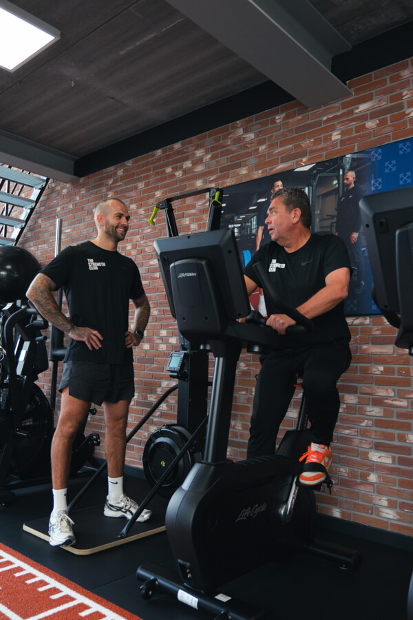 Personal trainer begeleidt een sporter op een home trainer