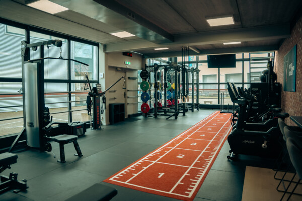 Trainingsruimte van The Strength Club met krachtapparatuur en een oranje sprintbaan