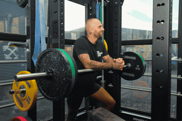Personal trainer leunt op een halterstang in het trainingsrek