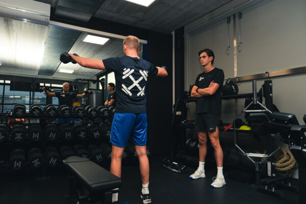 Sporter heft dumbbells zijwaarts onder begeleiding van een personal trainer